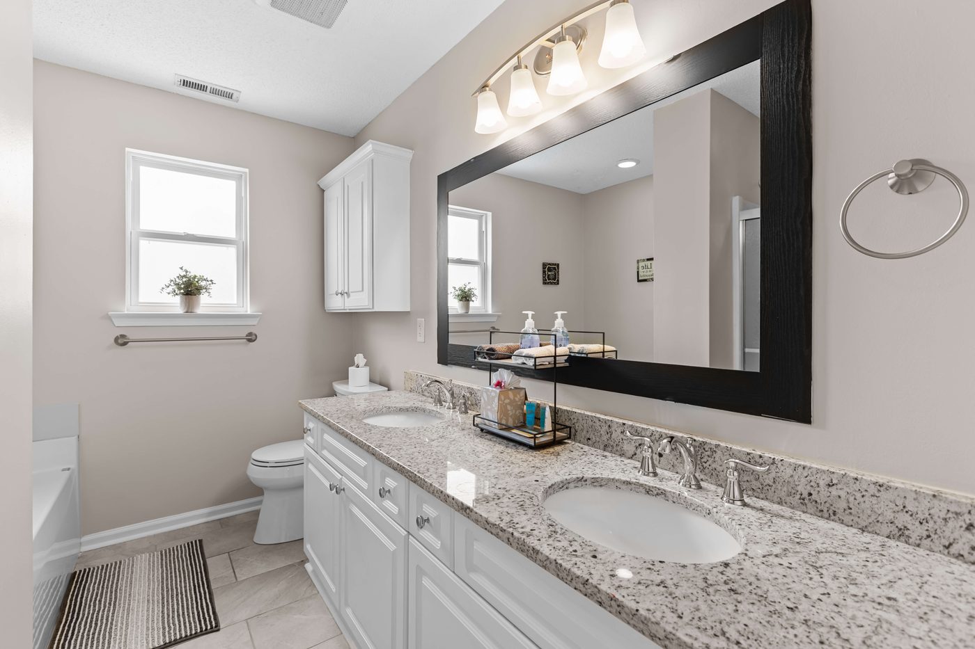 Primary ensuite bathroom with a double sink granite vanity and a large framed mirror